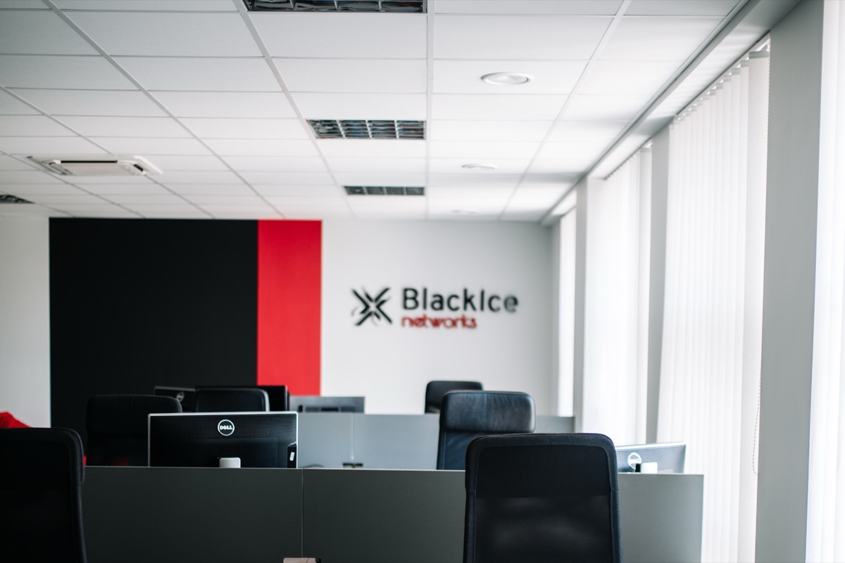Stanowiska pracy w biurze BlackIce Networks, w tle czerwono-czarna ściana z logo firmy